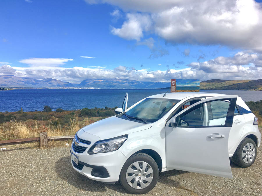 A photo of a car on a road trip parked with a lake in the background