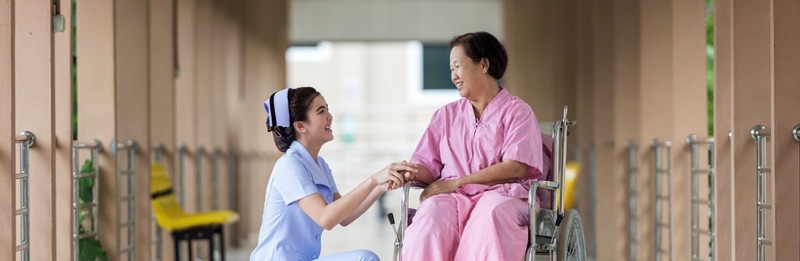 A nurse helping an elderly woman in a wheelchair. They are both smiling.