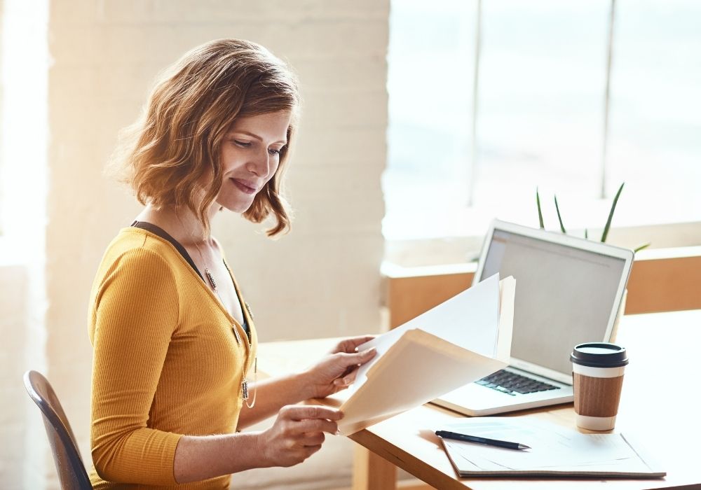 A woman working at a computer with a coffee and a folder with her job reports inside