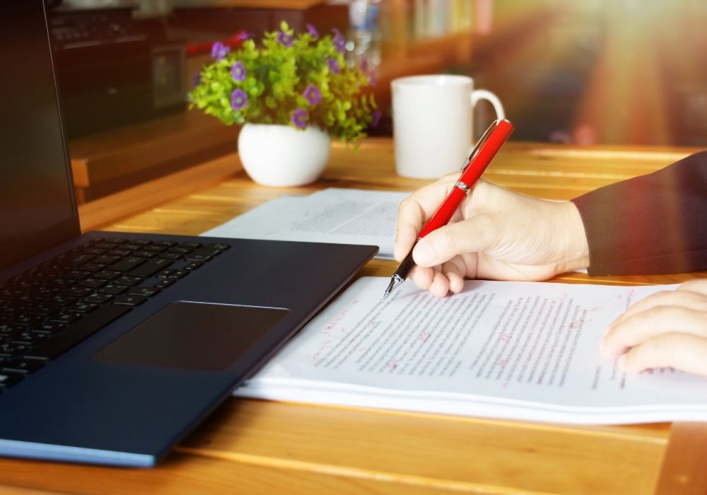 proofreading jobs from home no experience. woman writing at her desk with a pen, paper and a laptop open