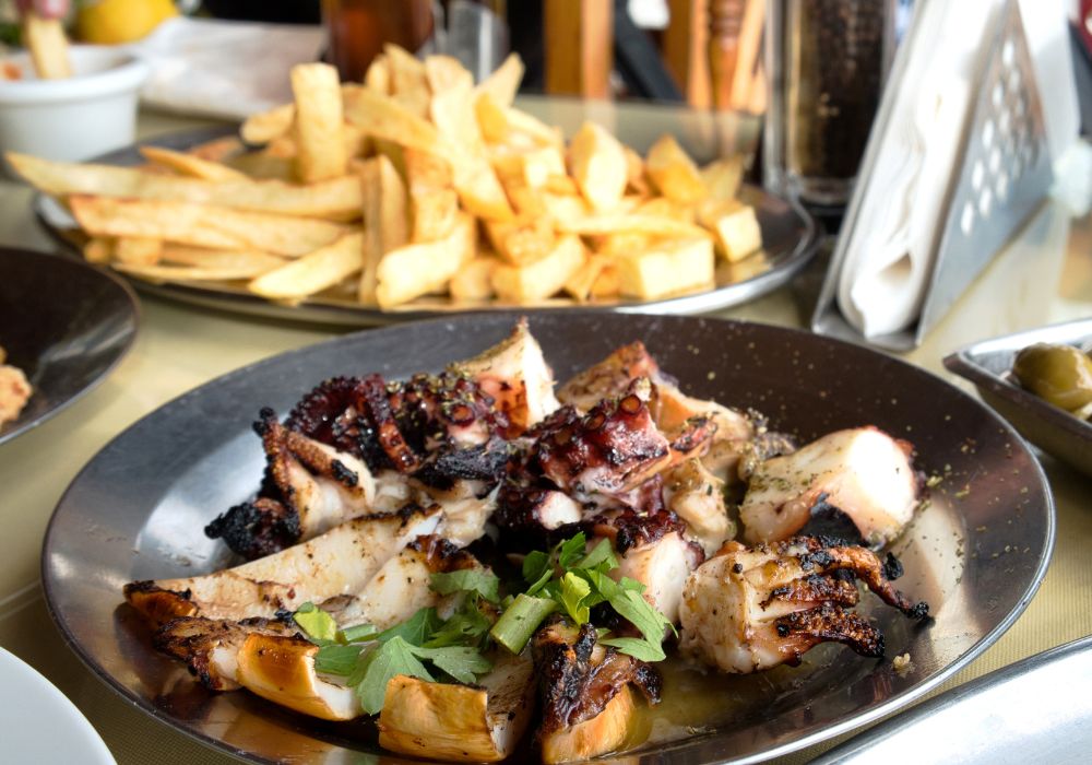 A marinated grilled seafood, french fries and vegetable salad with olive oil.