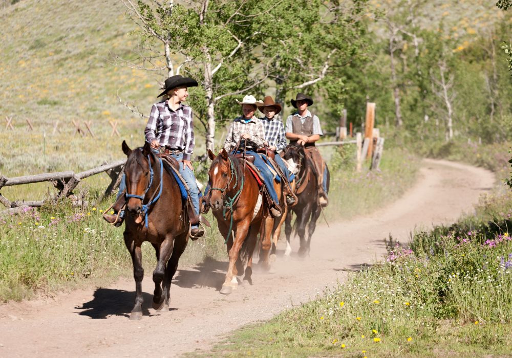 horseback riding tour in Bozeman MT with a guide and young kids riding behind on a dusty path