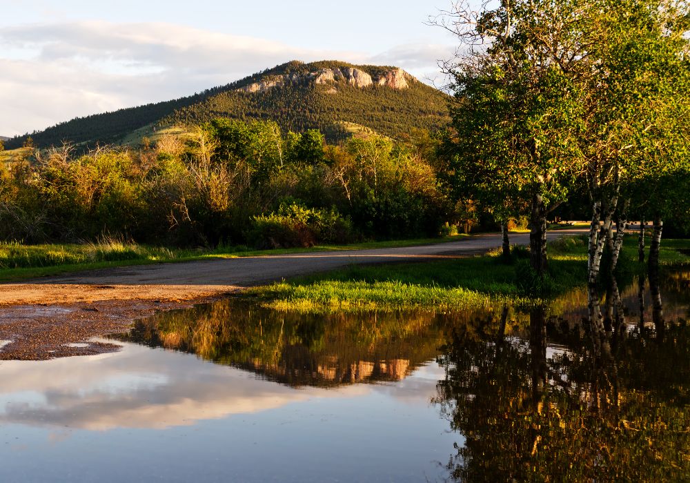 Mount Helena can be seen from many parts of Helena, Montana and a reflection of Mt Helena in calm water with a lush of green trees during sunset..