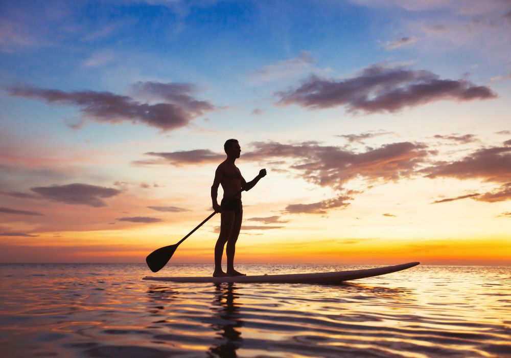 A beautiful silhouette of a man at sunset during stand-up paddle boarding.