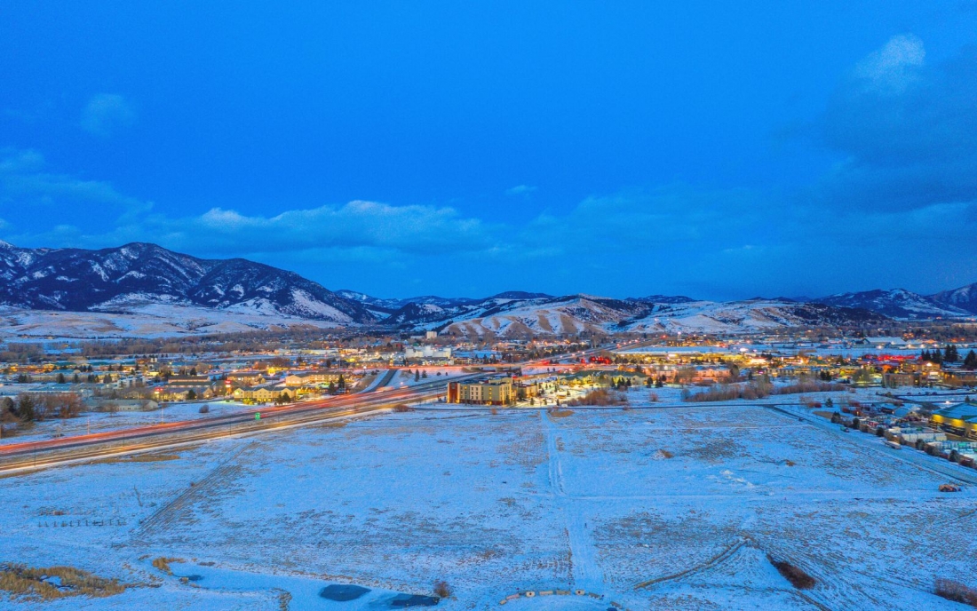 An aerial view of a snowy Bozeman, Montana at night with retail stores and residential neighborhoods.