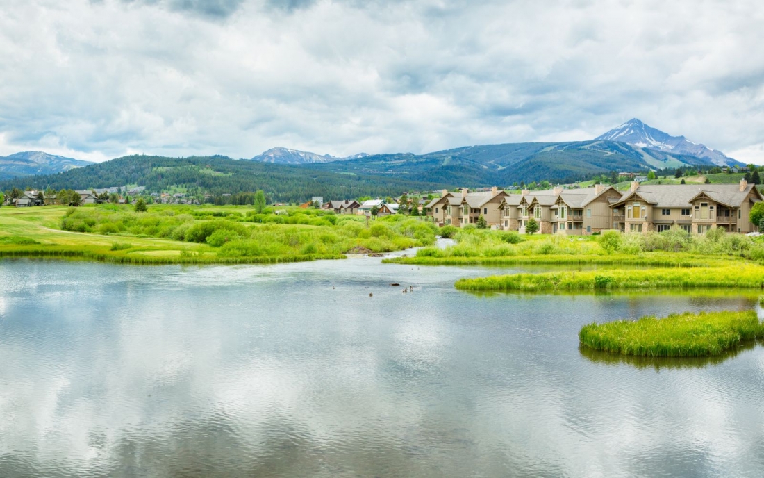 A panormic view of Big Sky, Montana with a pond, golf course, Lone Mountain and condos in the neighborhood.