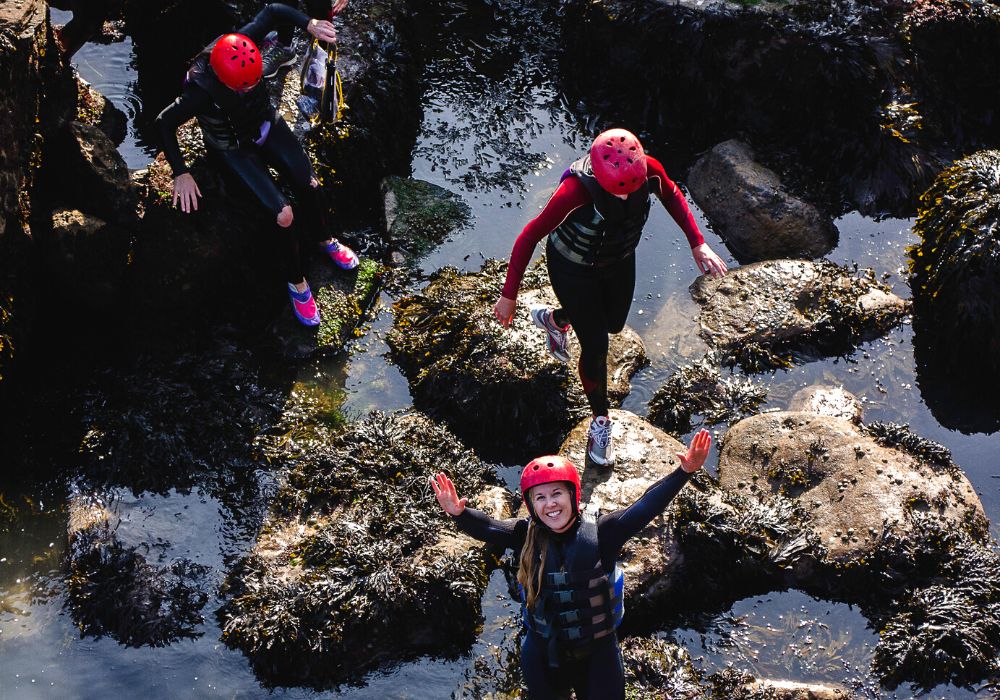 View from above of a group of friends walking on rocks next to the sea, and one woman is looking up.