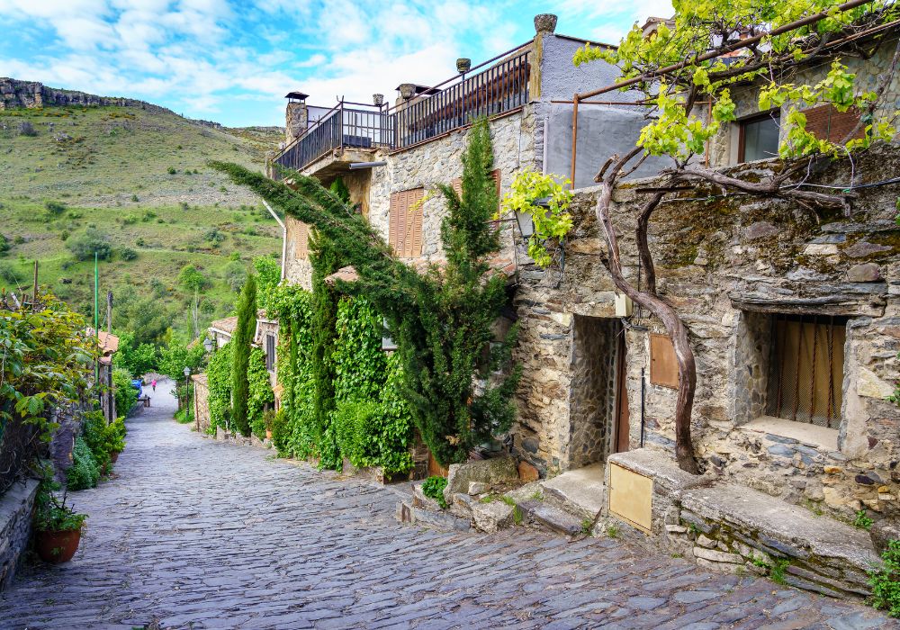 Old town street with mountain views, stone facades and green plants in Patones De Arriba, Madrid.