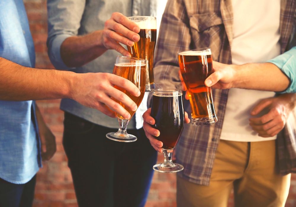 On a brick wall background, a male group clicks glasses of dark and light beer.
