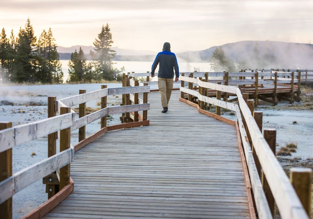 A man walks on a wooden boardwalk along geyser fields in Yellowstone National Park, USA.