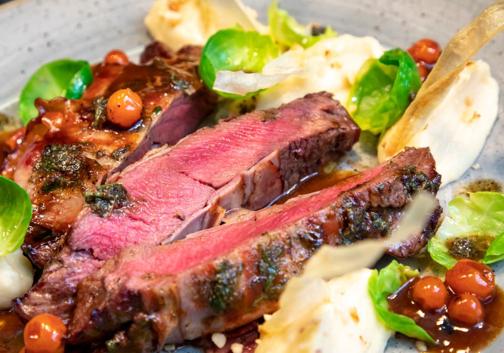 On a plate, a close-up of a rare venison steak fillet seasoned with fresh herbs and mashed.