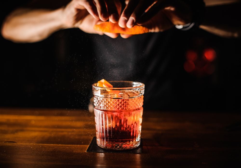 bartender with cocktail and orange peel preparing cocktail at bar