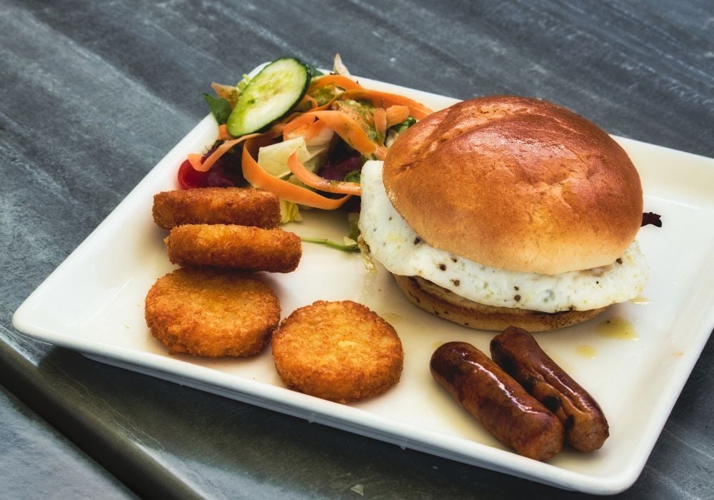 Breakfast brioche with fried egg, sausages, hash browns and salad