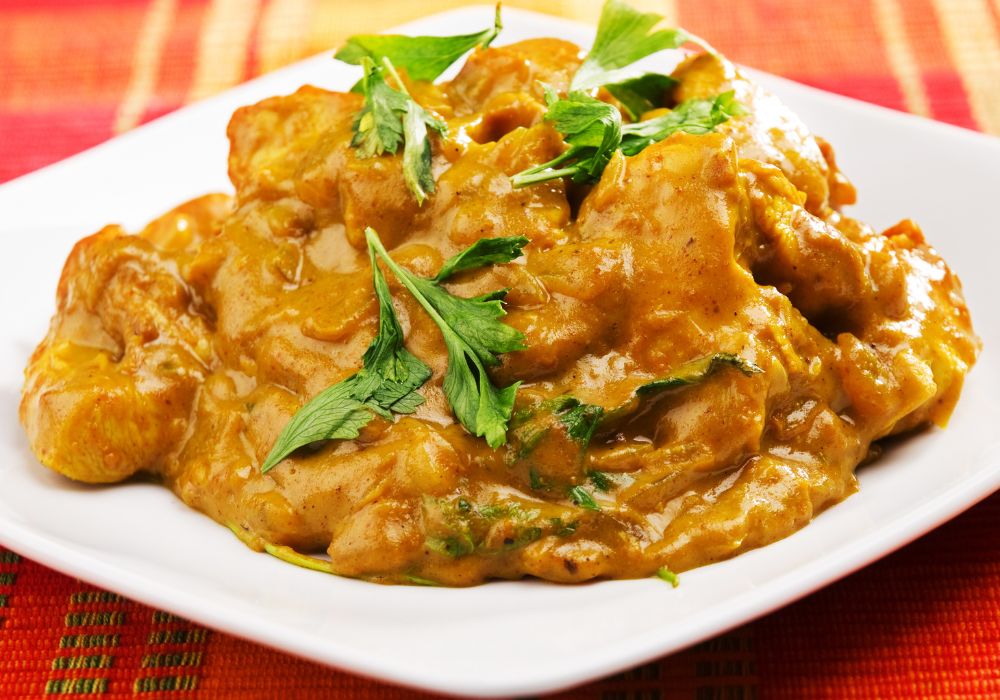 chicken tikka masala with herbs on top served on a color white plate