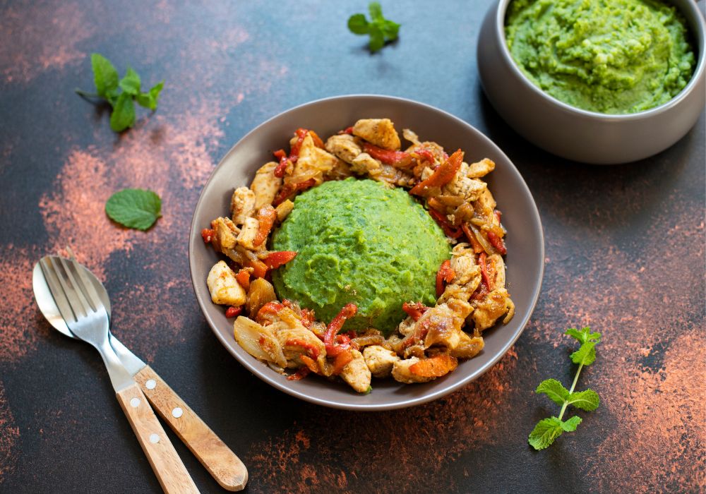 A close-up of mashed potatoes with green peas and corn served with chicken and vegetable stew. African cuisine, Kenyan cuisine, a traditional dish called mukimo or irio.