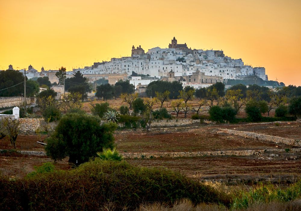 15 Greatest Issues To Do in Brindisi in 2023 16 Cityscape of Ostuni white town skyline at sunset with olive trees in the foreground during a orange-glowing sunset.
