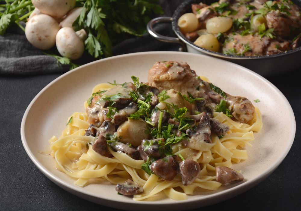 Fricassee is chicken stewed in a creamy sauce with mushrooms on a white plate on a black tablecloth.