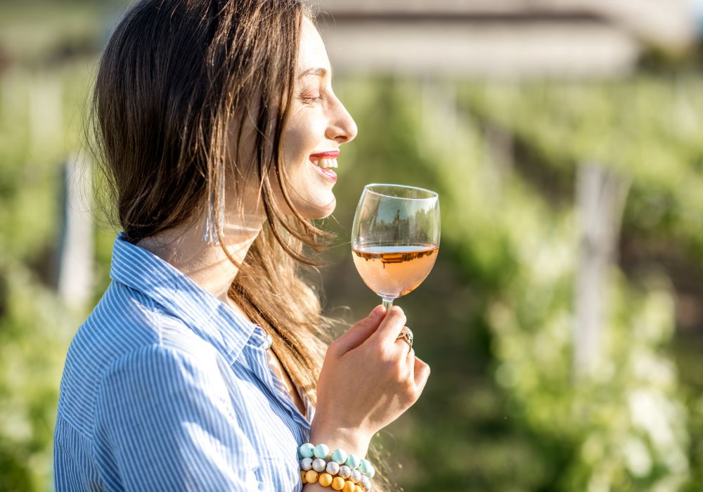 Young woman tasting wine standing outdoors on the vineyard in Bordeaux region during a sunset in France