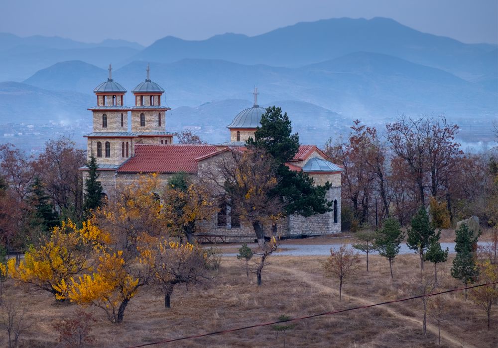 A church on top of a hill in Korce, Albania, with a view of the mountains that surround the city in the background.