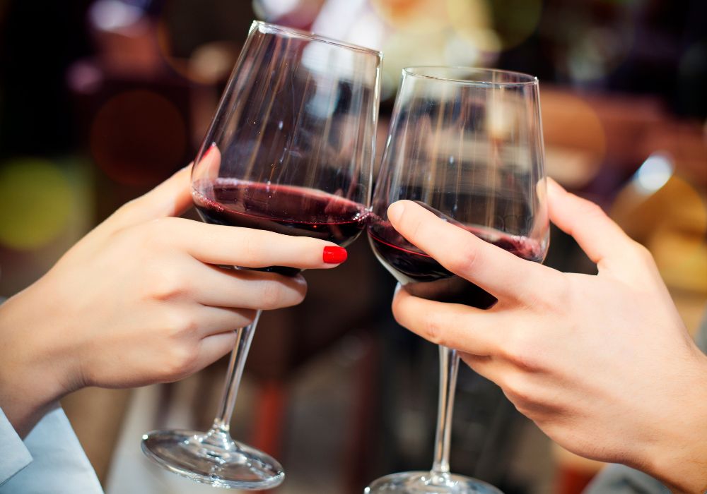 Two people toast with red wine at the bar.