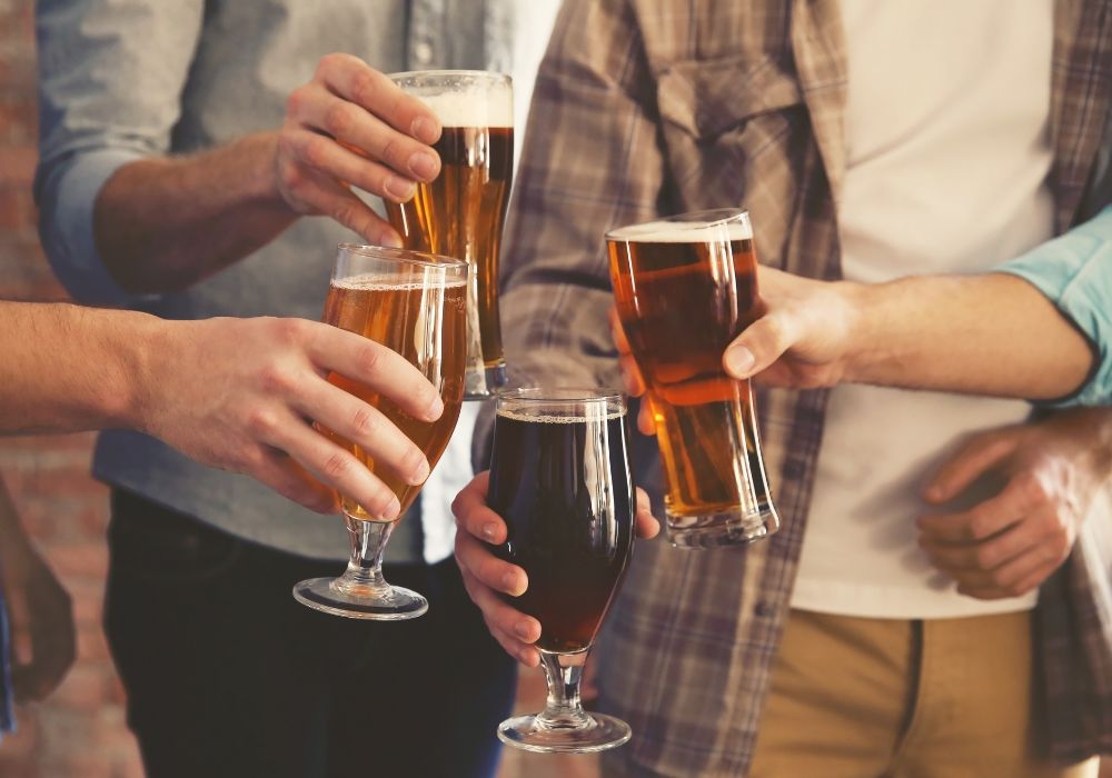 Male group clinking glasses of dark and light craft beer on a brick wall background