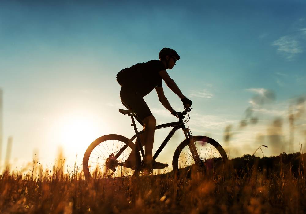 A man cycles at sunset in a grassy field.