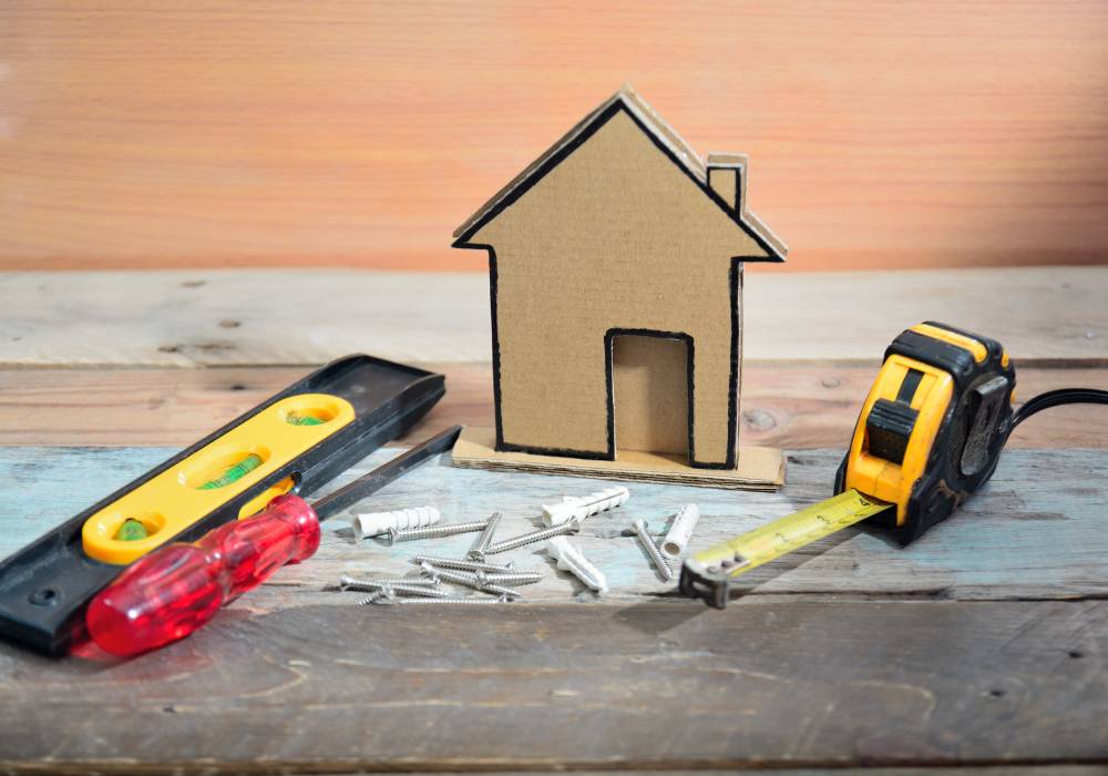 a cardboard house with tools around it illustrating the idea of home repair and maintenance on a niche website or blog.