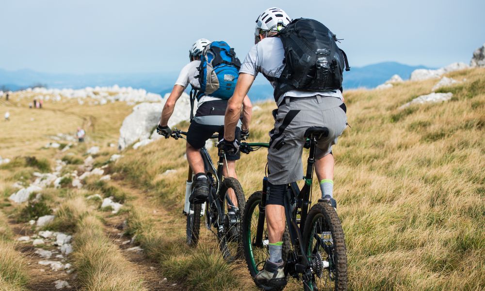 A couple rides mountain bikes on a narrow trail in a field near Bozeman Montana