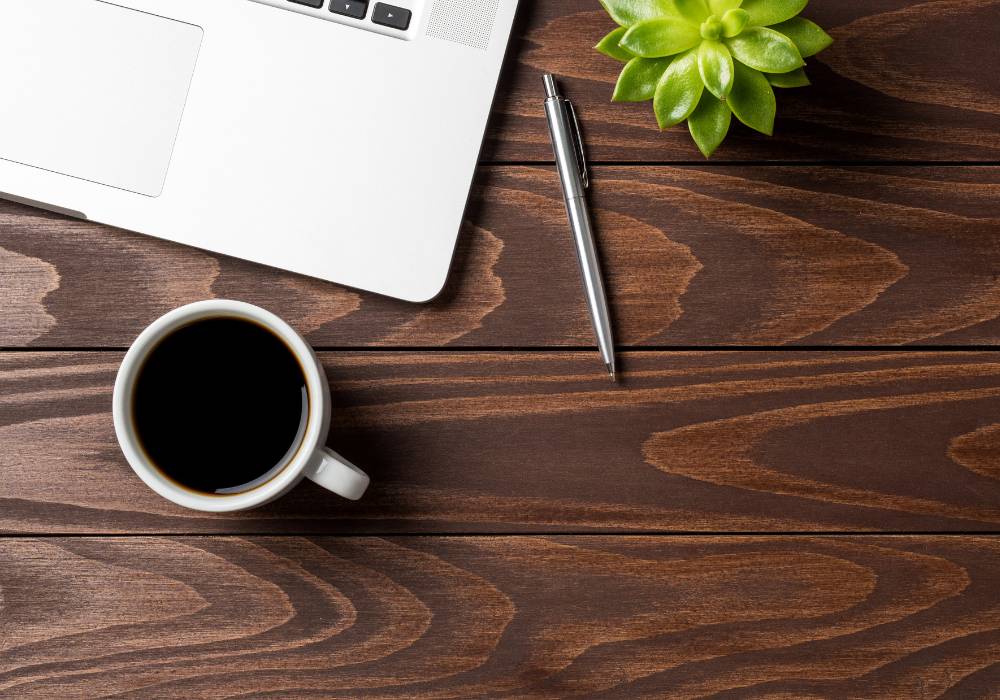 A photo of a laptop computer with a pen, plant and coffee on a dark wooden desktop