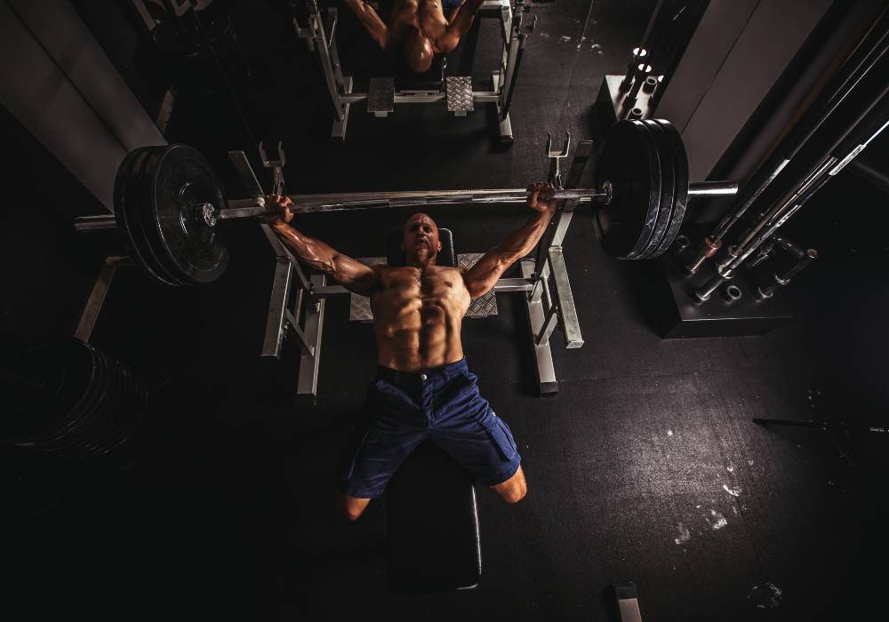 A photo of a strength training blogger from above while he does a bench press in a dark gym.