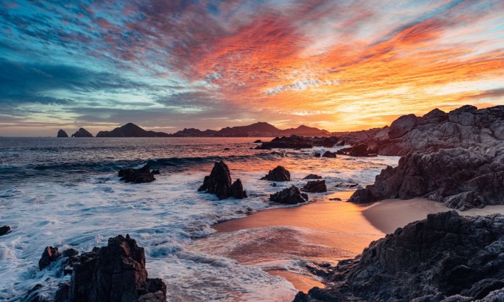 orange and red sun setting over the ocean in cabo san lucas, mexico