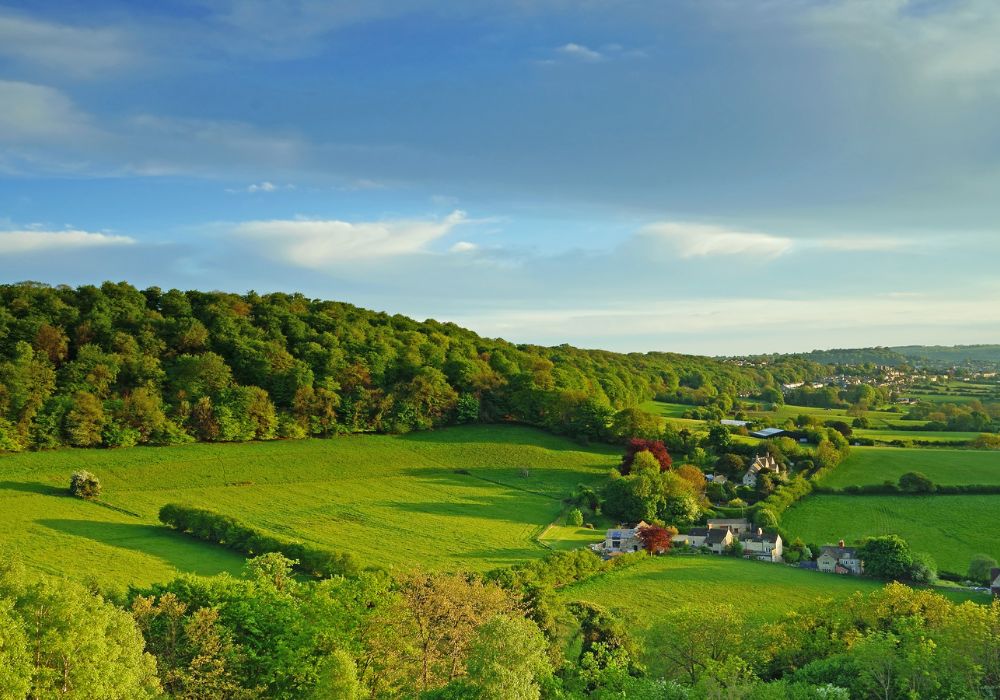 village of slad in the cotswolds with green farmland, trees and some homes