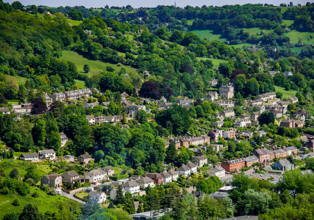 village of stroud in cotswolds england. many homes surrounded by green trees and hills