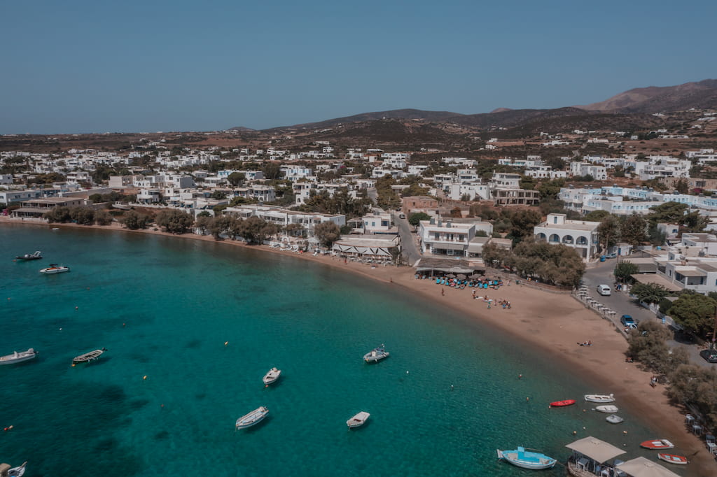 Alyki Beach with calm blue water and boats floating, small bay and white homes