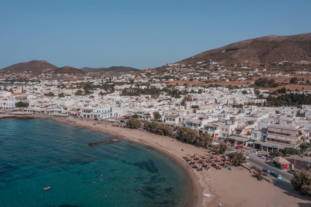 parikia beach in paros greece sandy cove with blue water and white homes climbing up the mountain