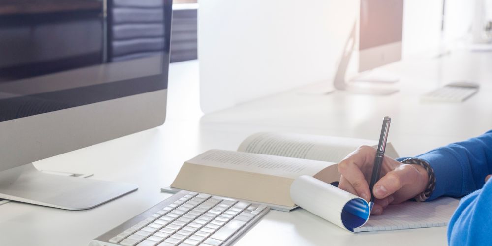 A man taking notes next to his computer working from home as a freelancer