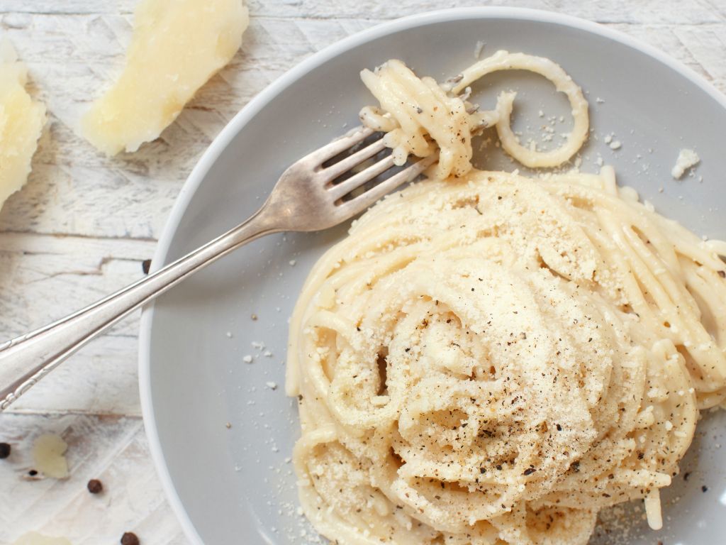 a plate with caccio e pepe sauce and a fork with spaghetti twirled around it