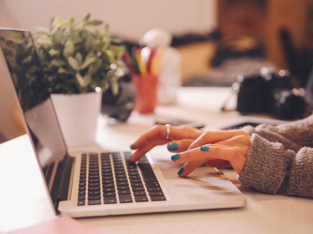 woman at her desk typing on a laptop with only her hands showing