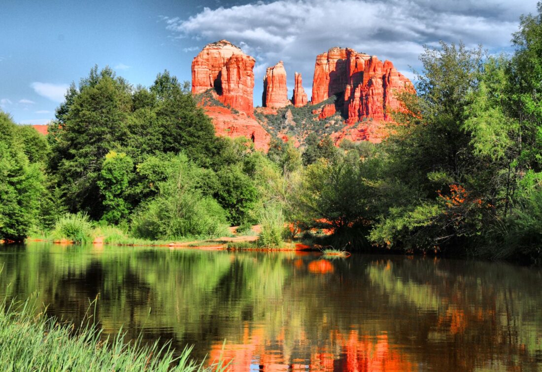 things to do in sedona visit the red rocks. jagged rocks with green trees and a river