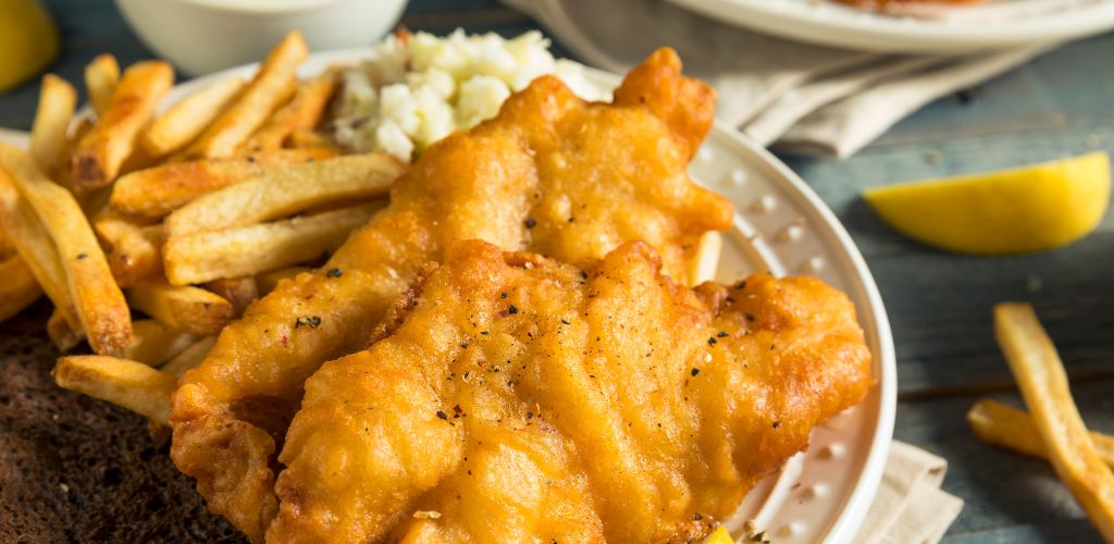 Beer-battered fish on a white plate with fries and lemons