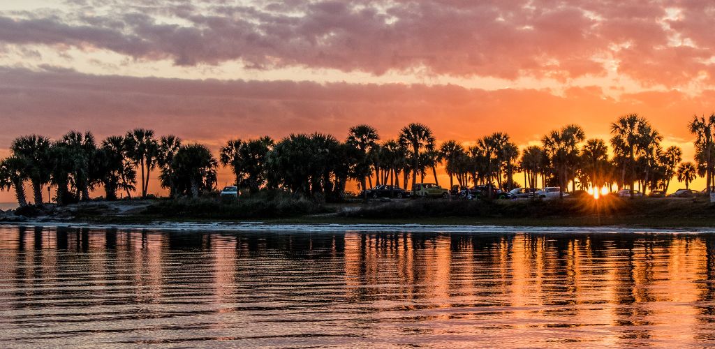 a setting sun with palm trees struck by sun rays