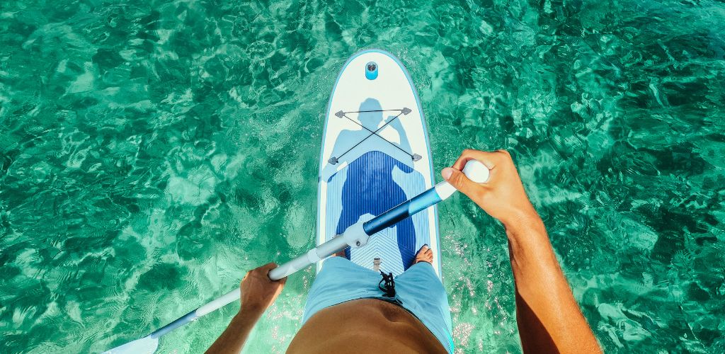 A photo of a POV view paddleboarding over crystal clear water.