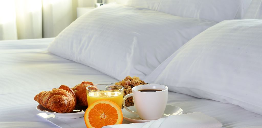 a bread, juice and coffee in the white bed  and a white pillow background