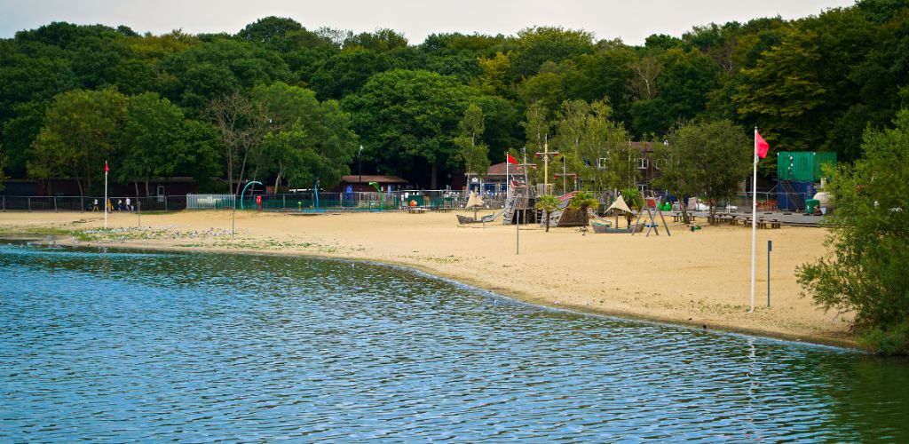 Ruislip Lido. Beach with trees, cottages and flags.