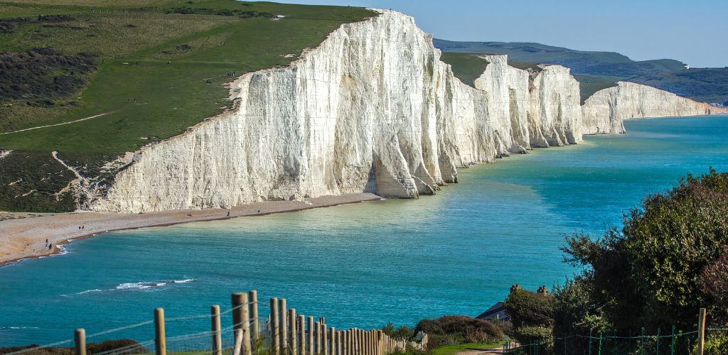 Seven Sisters and Friston Forest, a white  high cliff and the green grasses above it. Beneath the cliff is an ocean 