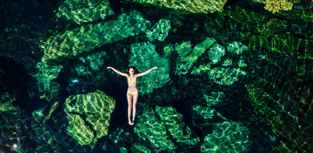 A woman in a bikini floating in the clear water of a cenote in Tulum