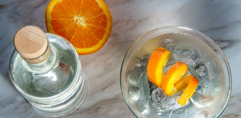 Gin martini on the rocks with orange peel twist and bottle in the background.