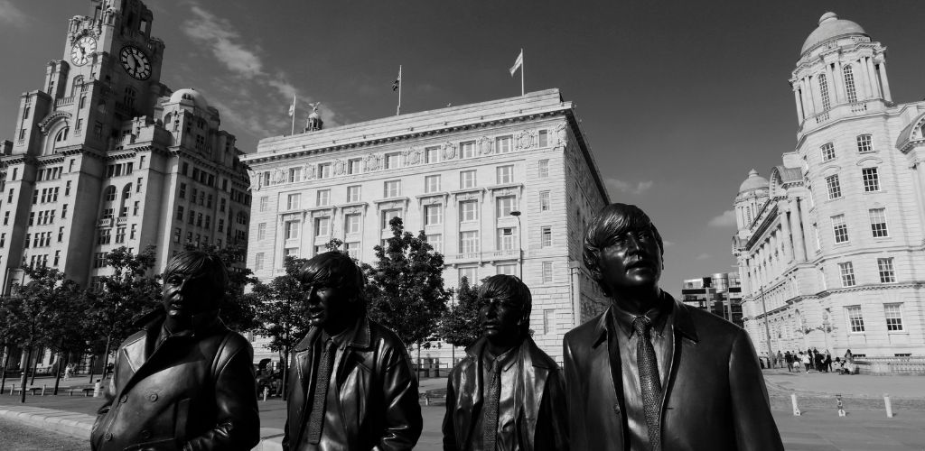 A black and white image of Beatles group statue and building structure at the background. 