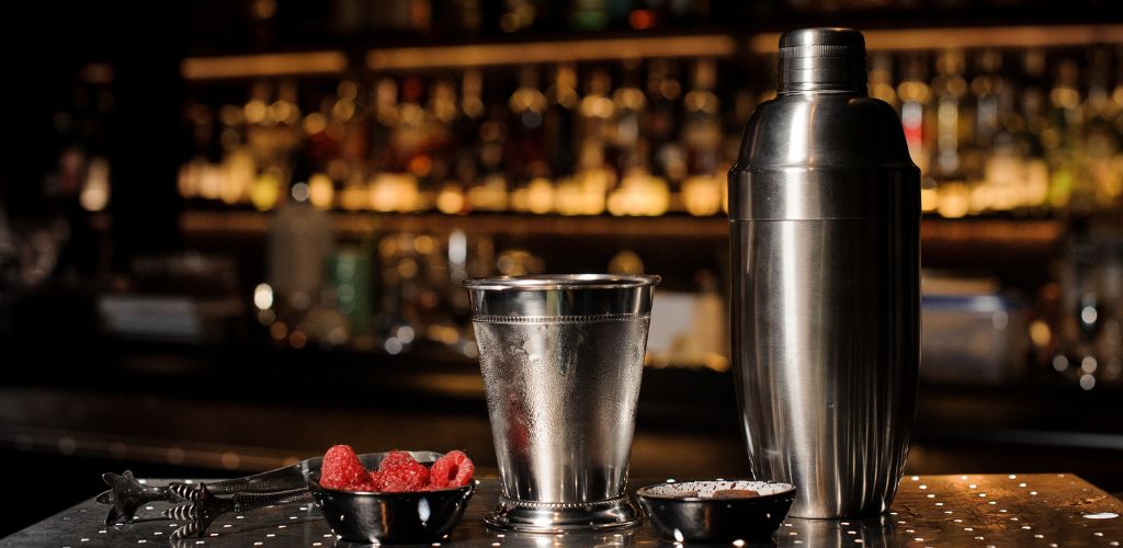 Professional bar equipment, shaker, glass and tongs arranged on the bar counter. 