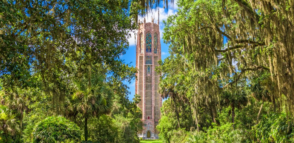 A tower in the middle of green plants and trees in the blue clear sky. 